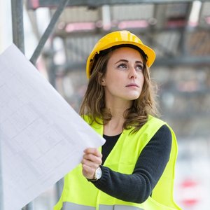 Eine Frau mit Bauhelm hält eine Zeichnung auf einer Baustelle