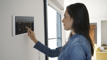 Eine Frau bedient eine Lüftung-Klima-App auf einem Display das an der Wand montiert ist, in einem Wohnzimmer.